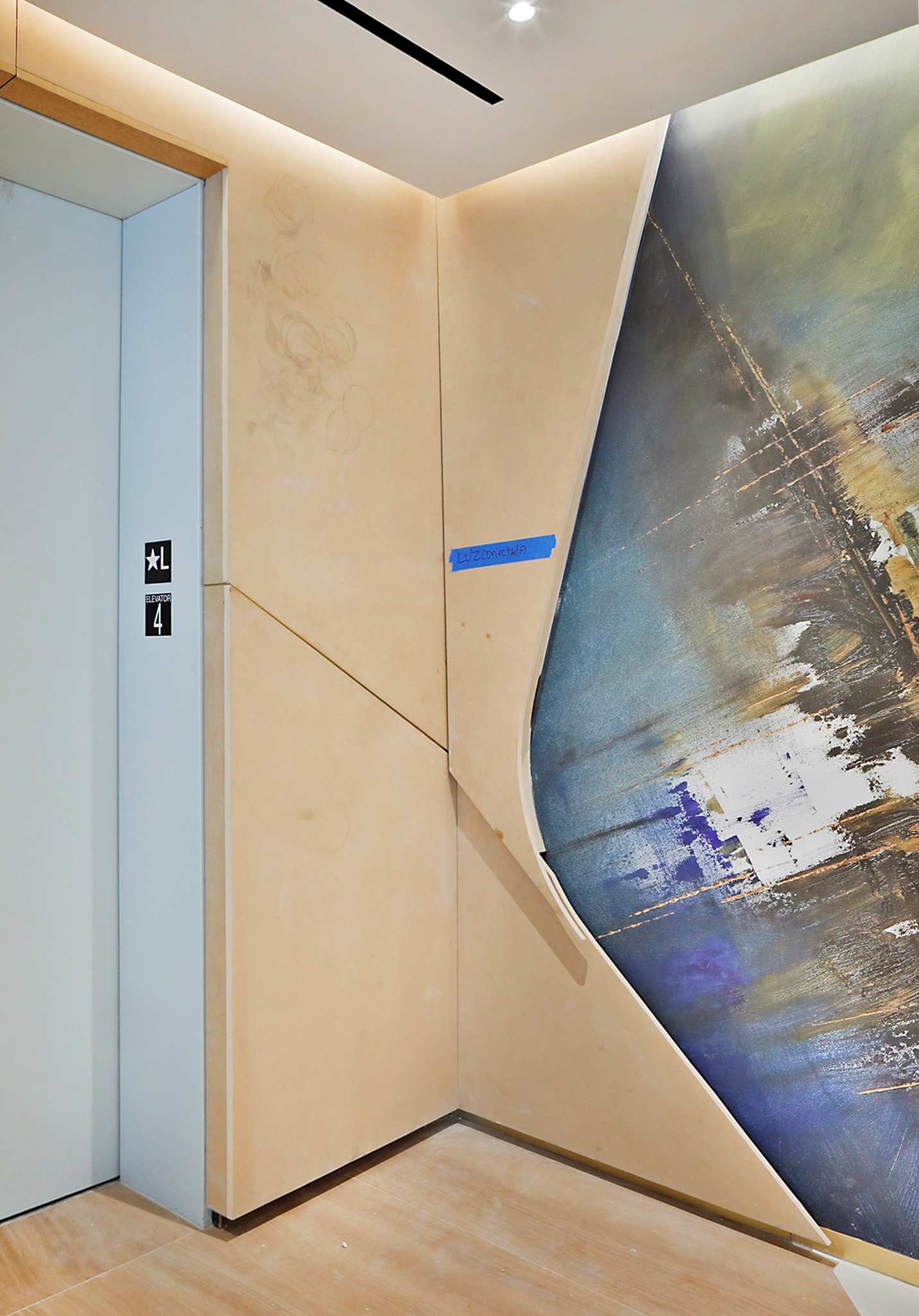 Elevator lobby corner before resurfacing, showing scuffed raw wall panels marked with painter's tape ahead of a DI-NOC architectural film installation